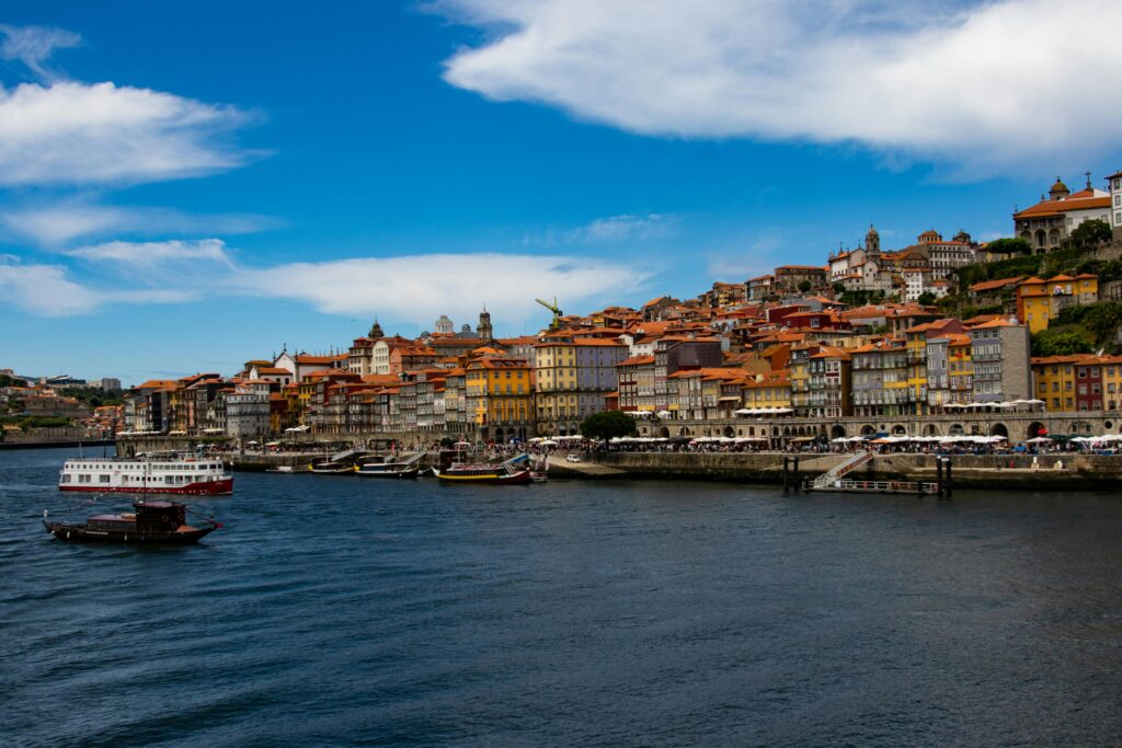 pexels-photo-2549156-2549156 Beautiful panoramic view of Porto's riverside with colorful buildings and boats under a vibrant blue sky.
