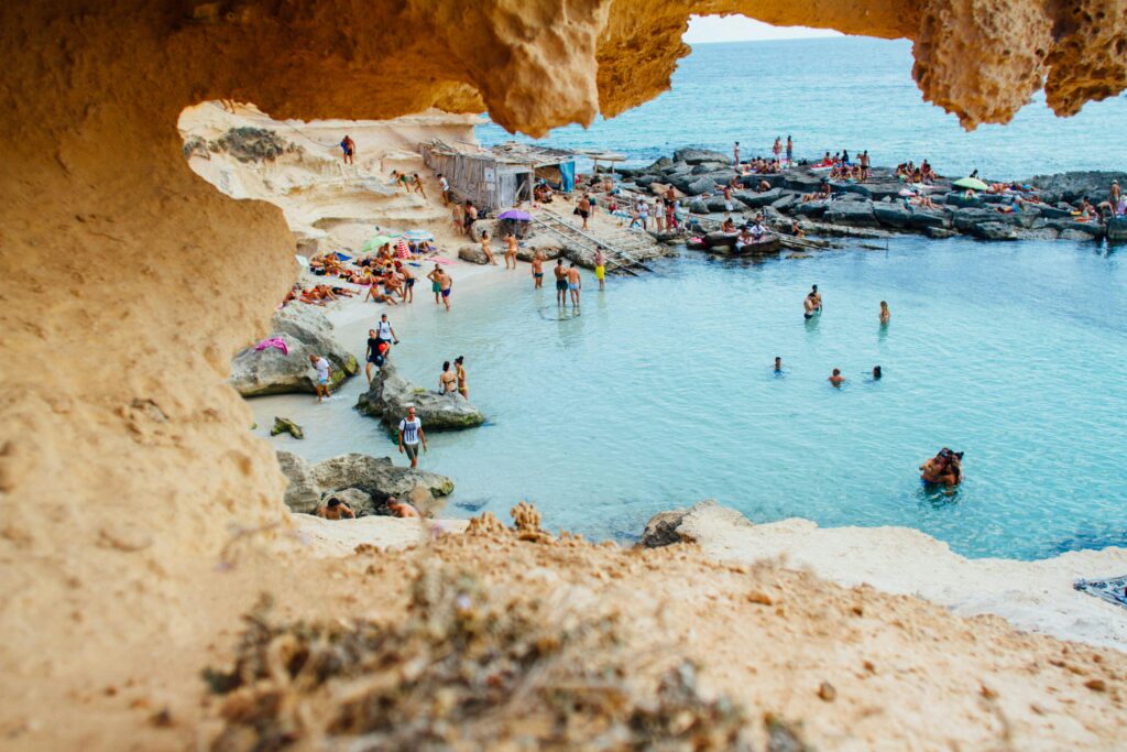 A picturesque beach scene in Spain with people enjoying swimming and sunbathing by rock formations. A picturesque beach scene in Spain with people enjoying swimming and sunbathing by rock formations.